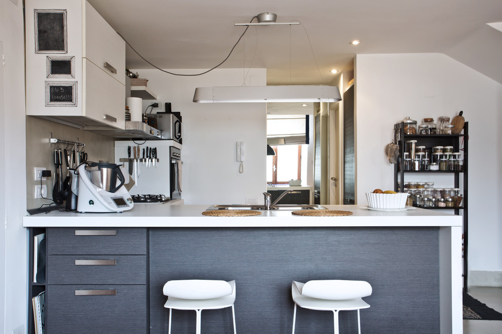 Small eclectic l-shaped eat-in kitchen in Naples with a double-bowl sink, grey cabinets, grey splashback, concrete floors, a peninsula, grey floor and white benchtop.
