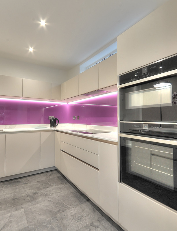 Modern eat-in kitchen in Other with a single-bowl sink, flat-panel cabinets, white cabinets, quartzite benchtops, glass sheet splashback, black appliances, vinyl floors, with island, grey floor, pink splashback and white benchtop.