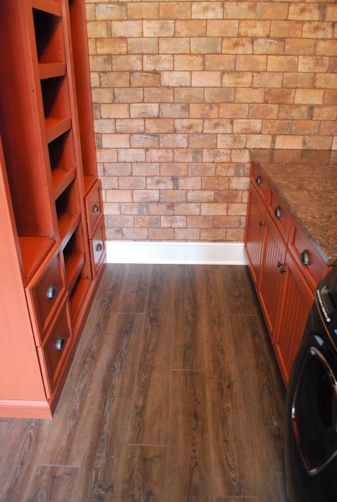 This is an example of a mid-sized contemporary l-shaped utility room in Cleveland with a farmhouse sink, shaker cabinets, medium wood cabinets, granite benchtops, vinyl floors and brown floor.