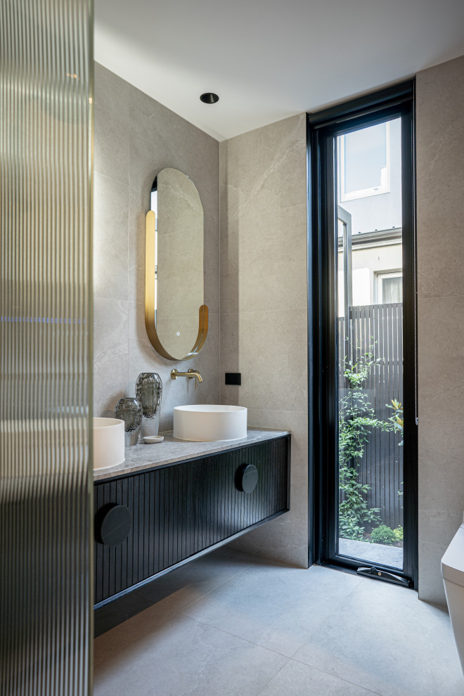 Cette image montre une salle de bain design de taille moyenne avec des portes de placard noires, un carrelage gris, une vasque, un sol gris, un plan de toilette gris, meuble double vasque, meuble-lavabo suspendu et un placard à porte plane.