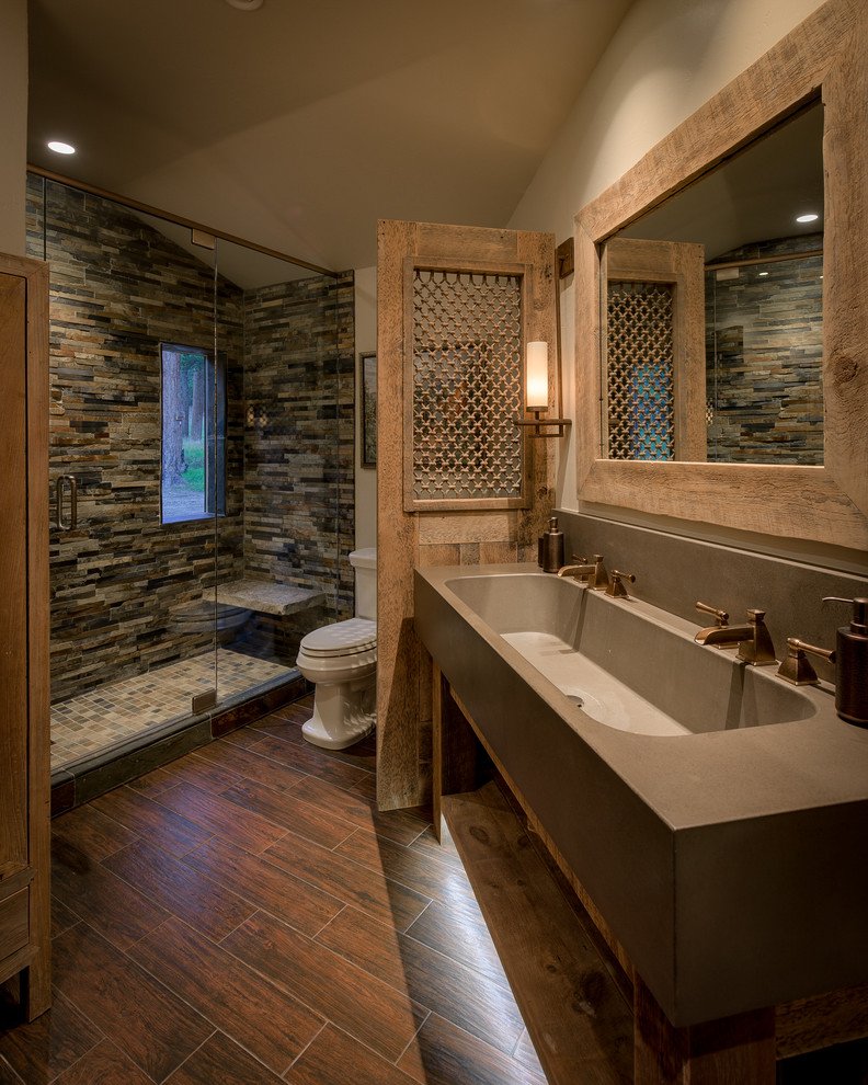 Mid-sized country 3/4 bathroom in Denver with furniture-like cabinets, medium wood cabinets, an alcove shower, a one-piece toilet, beige tile, stone tile, beige walls, dark hardwood floors, an integrated sink, concrete benchtops, brown floor and a hinged shower door.