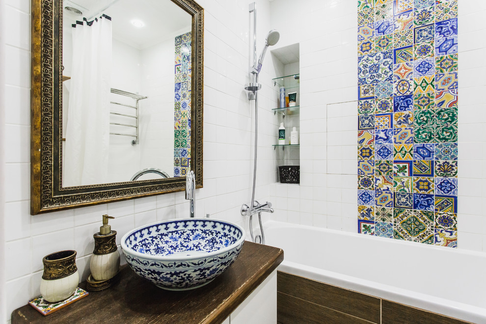 Photo of a small mediterranean master bathroom in Moscow with flat-panel cabinets, white cabinets, a shower/bathtub combo, multi-coloured tile, ceramic tile, white walls, a vessel sink, wood benchtops and brown benchtops.