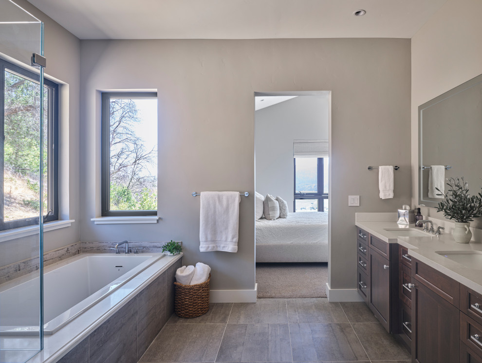 Photo of a medium sized rustic ensuite bathroom in San Francisco with shaker cabinets, a built-in bath, a shower/bath combination, beige walls, medium hardwood flooring, a submerged sink, engineered stone worktops, a hinged door, double sinks, dark wood cabinets, grey floors, white worktops and a freestanding vanity unit.