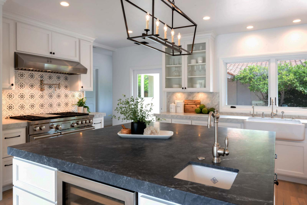 Photo of a contemporary l-shaped kitchen/diner in Santa Barbara with a belfast sink, white cabinets, marble worktops, grey splashback, marble splashback, white appliances, an island and grey worktops.