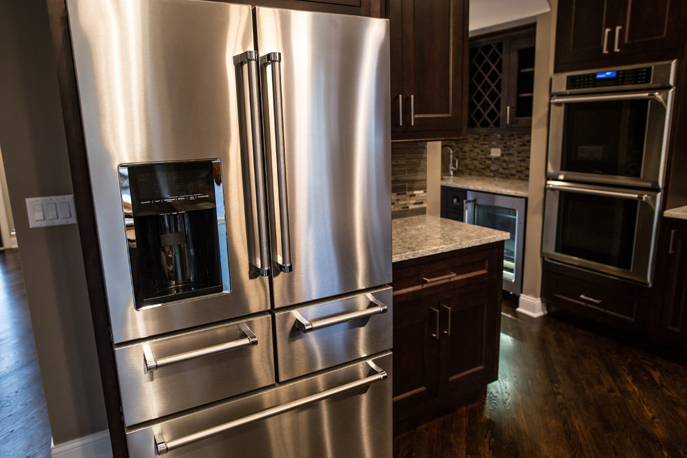 Mid-sized transitional l-shaped dark wood floor eat-in kitchen photo in Chicago with an undermount sink, shaker cabinets, brown cabinets, granite countertops, gray backsplash, subway tile backsplash, stainless steel appliances and an island
