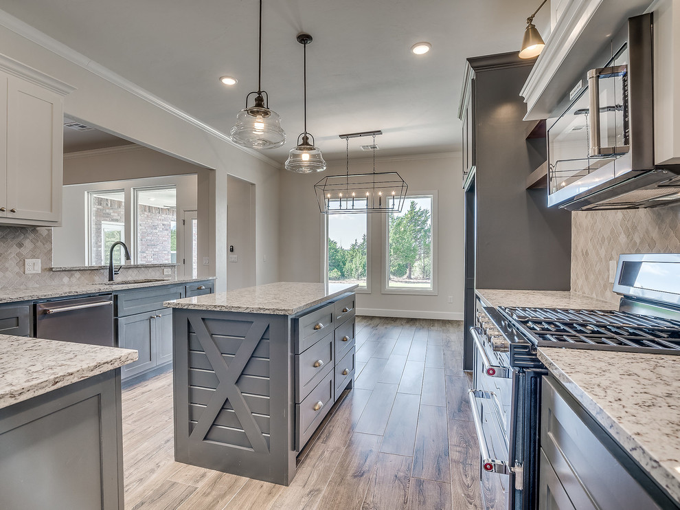 This is an example of an expansive country u-shaped eat-in kitchen in Oklahoma City with an undermount sink, shaker cabinets, grey cabinets, granite benchtops, multi-coloured splashback, marble splashback, stainless steel appliances, light hardwood floors, with island and multi-coloured benchtop.