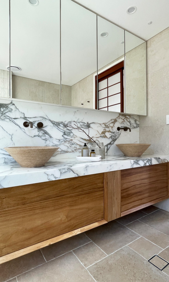 Large contemporary master bathroom in Sydney with furniture-like cabinets, medium wood cabinets, a freestanding tub, an open shower, a one-piece toilet, beige tile, porcelain tile, porcelain floors, a vessel sink, marble benchtops, white benchtops, a niche, a double vanity and a floating vanity.