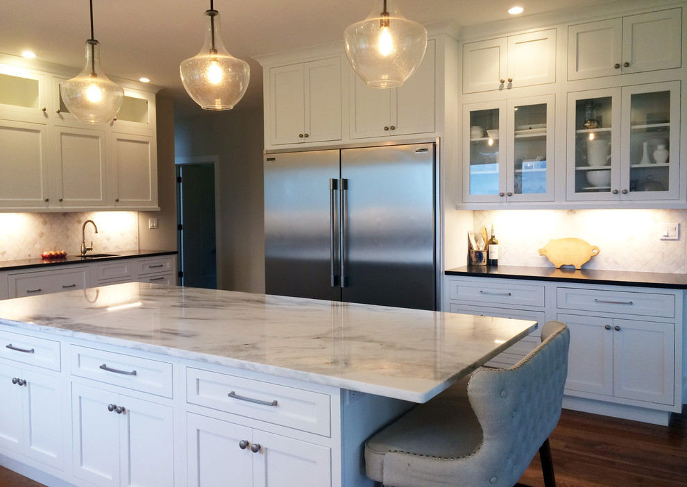 Inspiration for a large transitional l-shaped dark wood floor and brown floor kitchen pantry remodel with a farmhouse sink, recessed-panel cabinets, white cabinets, quartz countertops, beige backsplash, ceramic backsplash, stainless steel appliances, an island and black countertops