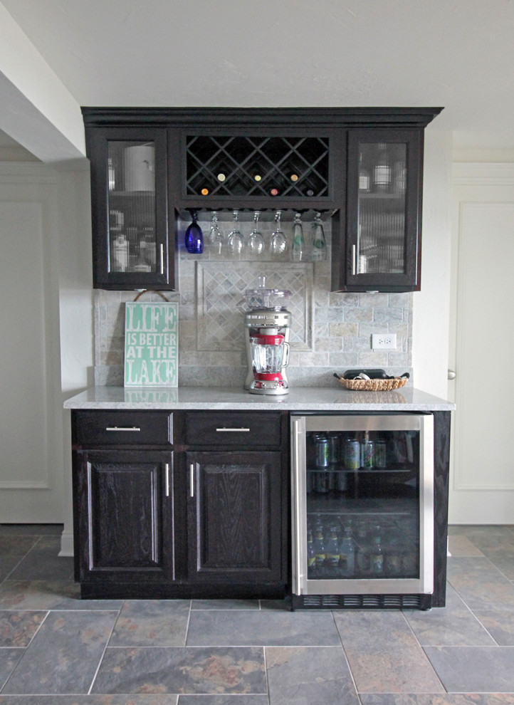Mid-sized country single-wall home bar in Milwaukee with recessed-panel cabinets, dark wood cabinets, quartz benchtops, grey splashback, stone tile splashback and slate floors.