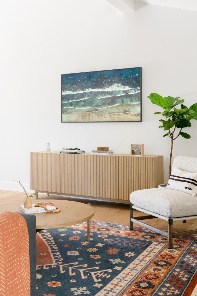 Inredning av ett minimalistiskt mellanstort allrum med öppen planlösning, med vita väggar, ljust trägolv, en standard öppen spis, en spiselkrans i gips, en väggmonterad TV och brunt golv