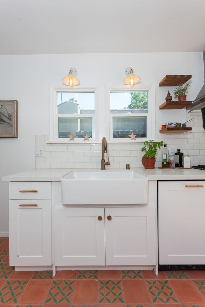 Photo of a mid-sized traditional galley separate kitchen in Los Angeles with a farmhouse sink, shaker cabinets, white cabinets, quartz benchtops, white splashback, subway tile splashback, stainless steel appliances, cement tiles, red floor and white benchtop.