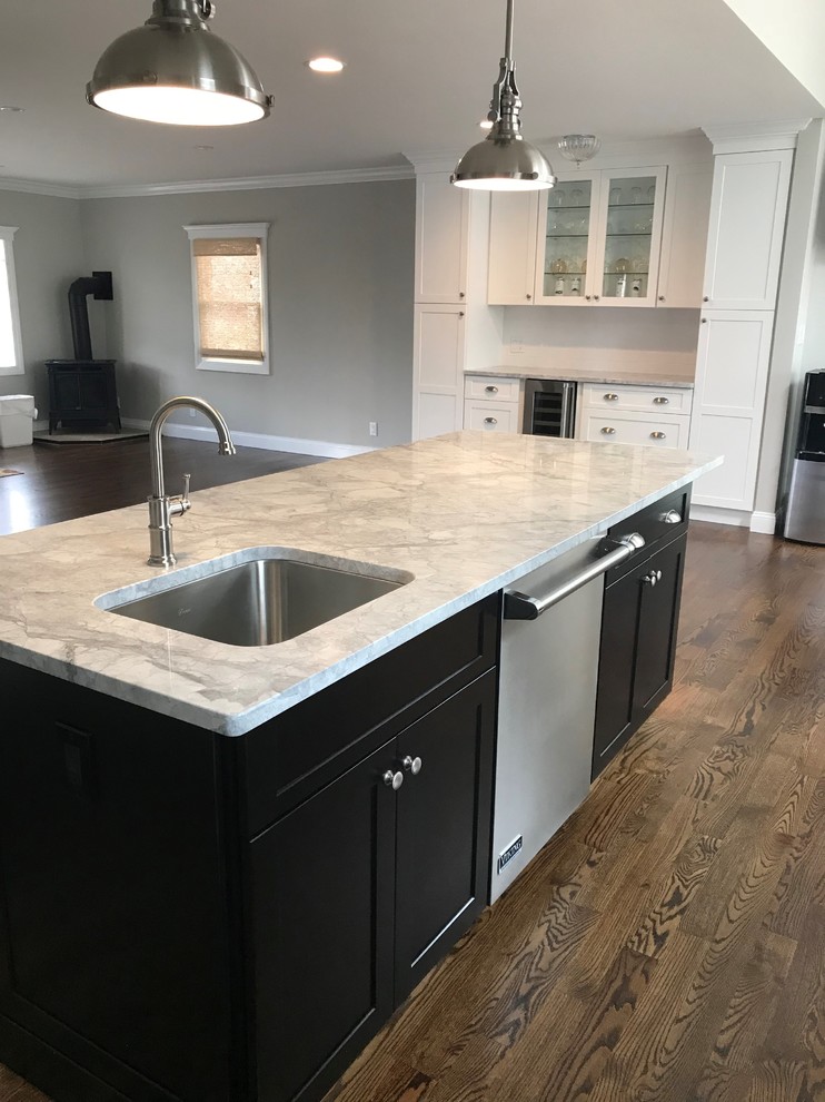 Mid-sized transitional u-shaped dark wood floor and brown floor eat-in kitchen photo in New York with a farmhouse sink, recessed-panel cabinets, white cabinets, wood countertops, white backsplash, limestone backsplash, stainless steel appliances, an island and gray countertops