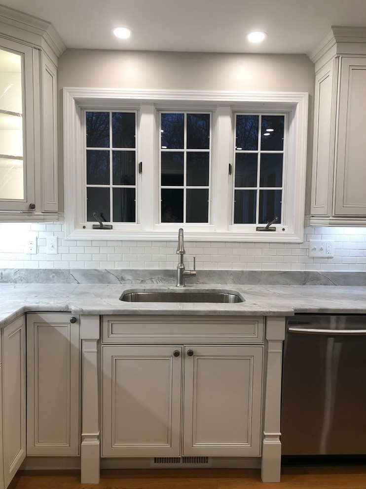 Open concept kitchen - large transitional l-shaped medium tone wood floor and brown floor open concept kitchen idea in Boston with an undermount sink, recessed-panel cabinets, white cabinets, quartz countertops, white backsplash, subway tile backsplash, stainless steel appliances, an island and multicolored countertops