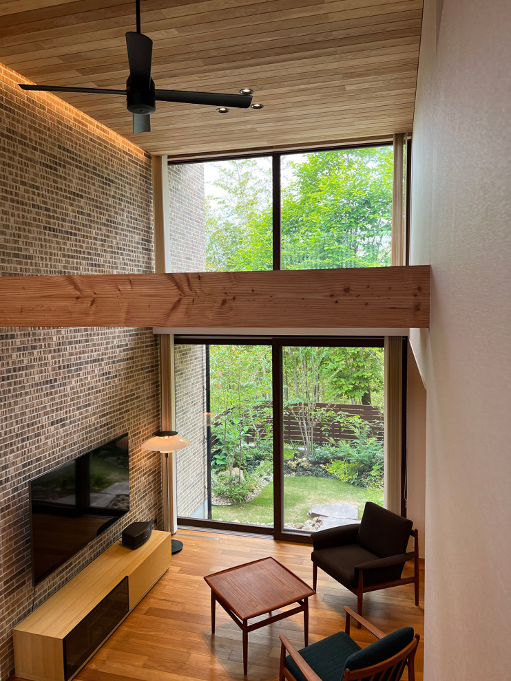 Imagen de biblioteca en casa abierta minimalista grande con suelo de madera en tonos medios, televisor colgado en la pared, suelo marrón, machihembrado y ladrillo