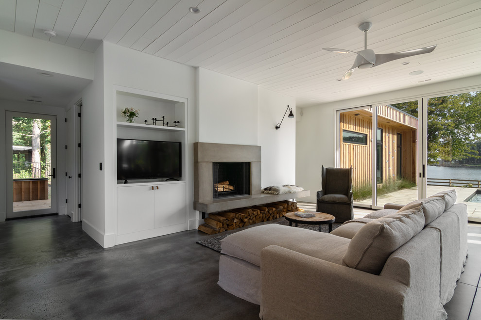 Inspiration for a large scandinavian open concept family room in Charlotte with white walls, concrete floors, a concrete fireplace surround and grey floor.