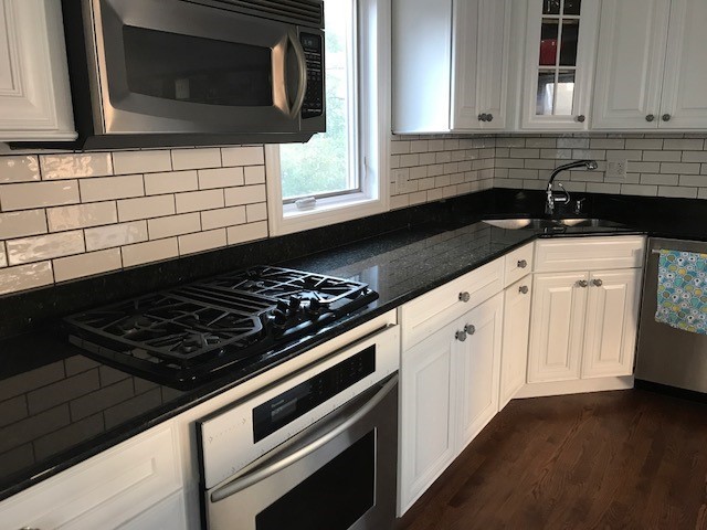 Inspiration for a large contemporary u-shaped dark wood floor kitchen remodel in Chicago with a drop-in sink, white cabinets, granite countertops, white backsplash, ceramic backsplash, stainless steel appliances and an island