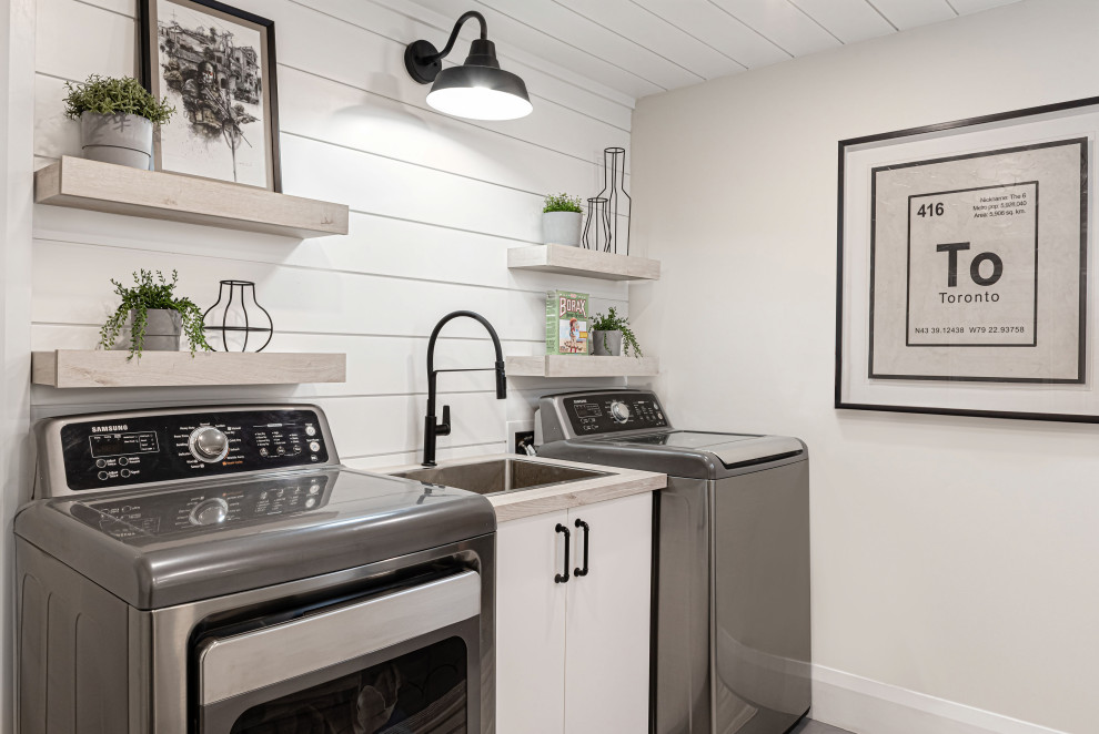 Inspiration for a mid-sized country dedicated laundry room in Toronto with a drop-in sink, flat-panel cabinets, white cabinets, laminate benchtops, grey walls, porcelain floors, a side-by-side washer and dryer, grey floor and timber.