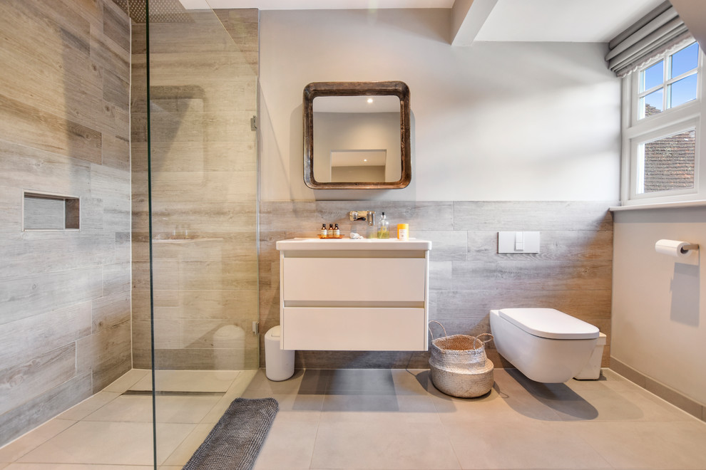This is an example of a transitional 3/4 bathroom in Surrey with flat-panel cabinets, white cabinets, a curbless shower, a wall-mount toilet, beige walls, an integrated sink, beige floor, an open shower and gray tile.