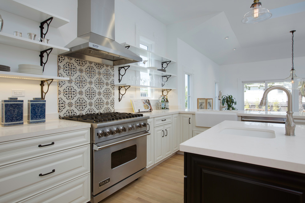Mid-sized transitional u-shaped kitchen in San Francisco with a farmhouse sink, raised-panel cabinets, white cabinets, limestone benchtops, white splashback, stainless steel appliances, light hardwood floors, with island and beige floor.