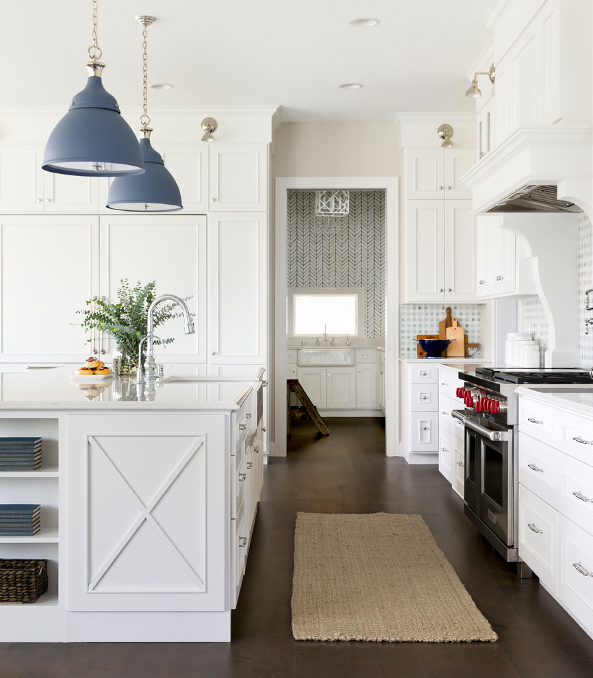 This is an example of a large beach style l-shaped eat-in kitchen in Minneapolis with a farmhouse sink, flat-panel cabinets, white cabinets, solid surface benchtops, blue splashback, mosaic tile splashback, stainless steel appliances, dark hardwood floors, with island and brown floor.
