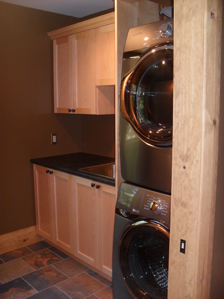 This is an example of a mid-sized traditional galley dedicated laundry room in Toronto with a drop-in sink, flat-panel cabinets, light wood cabinets, laminate benchtops, slate floors and a stacked washer and dryer.