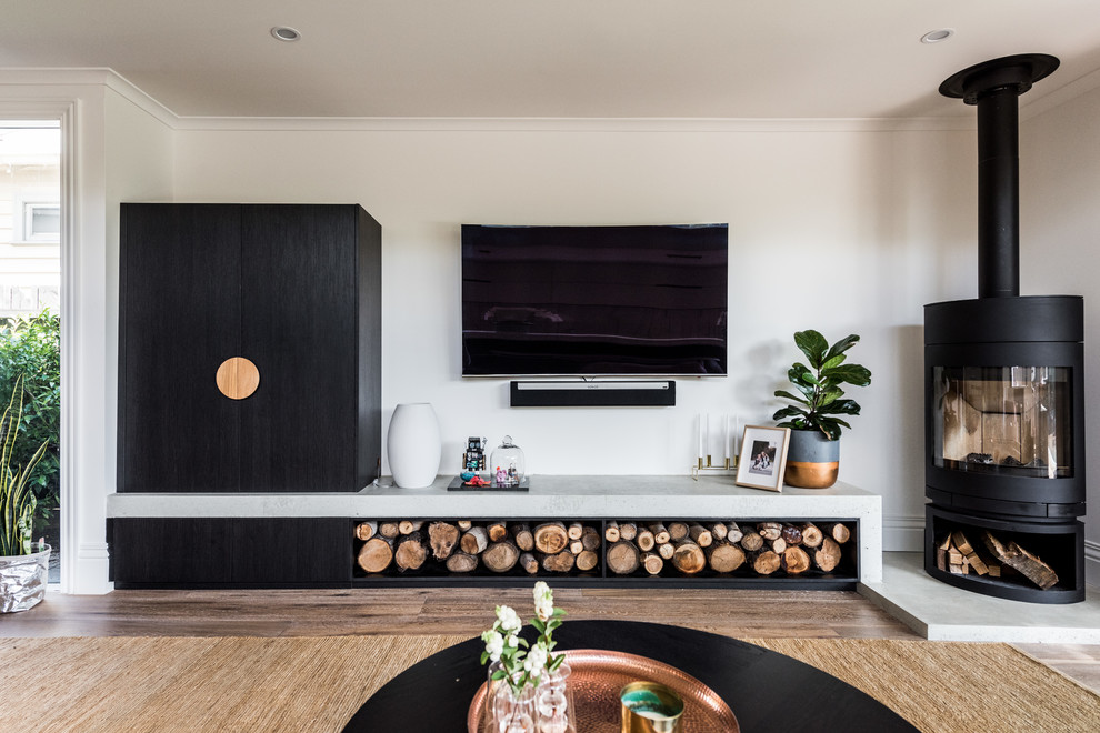 Photo of a modern formal open concept living room in Melbourne with white walls, medium hardwood floors, a wood stove, a metal fireplace surround, a wall-mounted tv and brown floor.