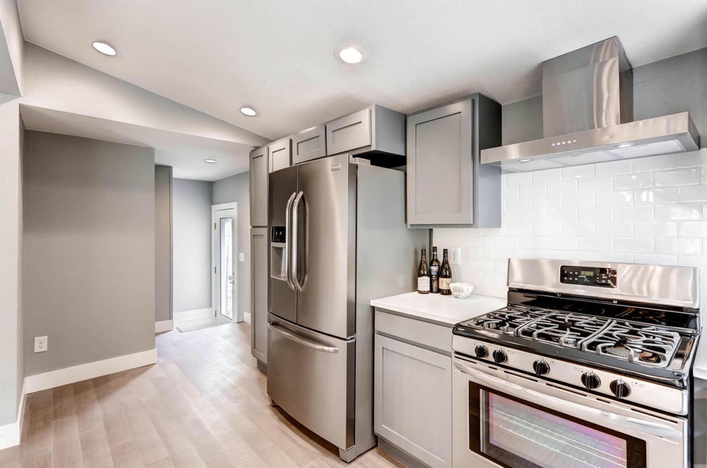Inspiration for a mid-sized transitional single-wall light wood floor and brown floor enclosed kitchen remodel with an undermount sink, recessed-panel cabinets, gray cabinets, quartz countertops, white backsplash, subway tile backsplash, stainless steel appliances and a peninsula