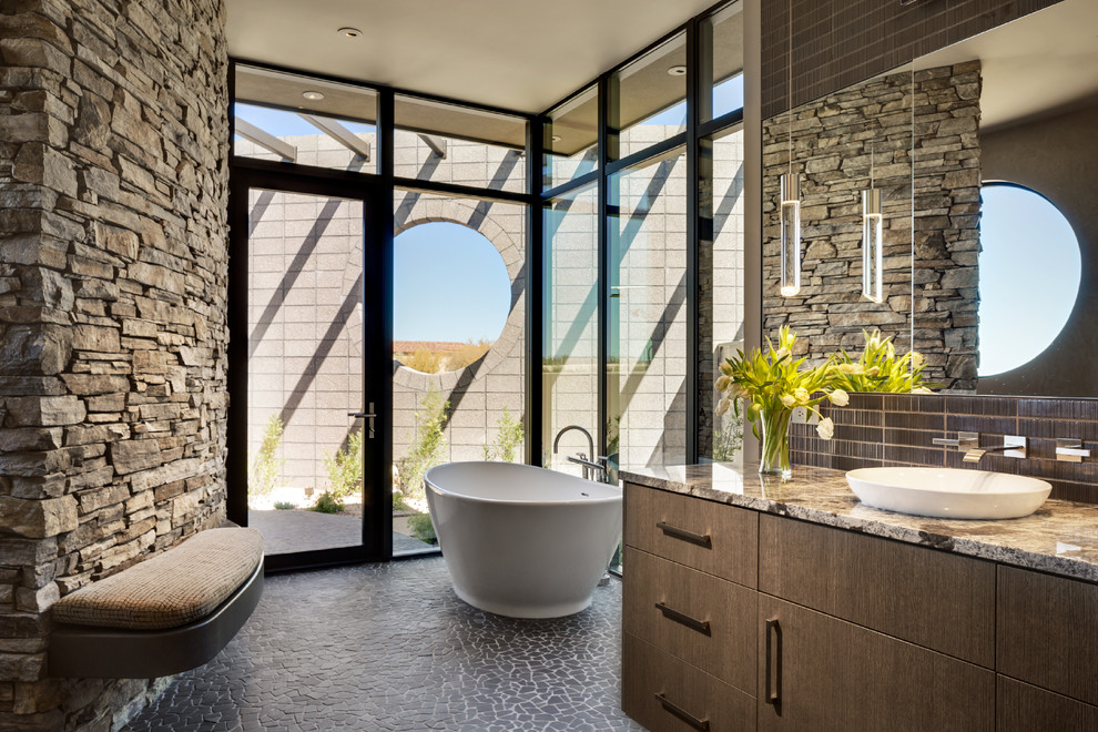 Inspiration for a mid-sized contemporary master bathroom in Phoenix with flat-panel cabinets, medium wood cabinets, a freestanding tub, an open shower, brown tile, ceramic tile, white walls, pebble tile floors, a vessel sink, granite benchtops, grey floor, an open shower and brown benchtops.