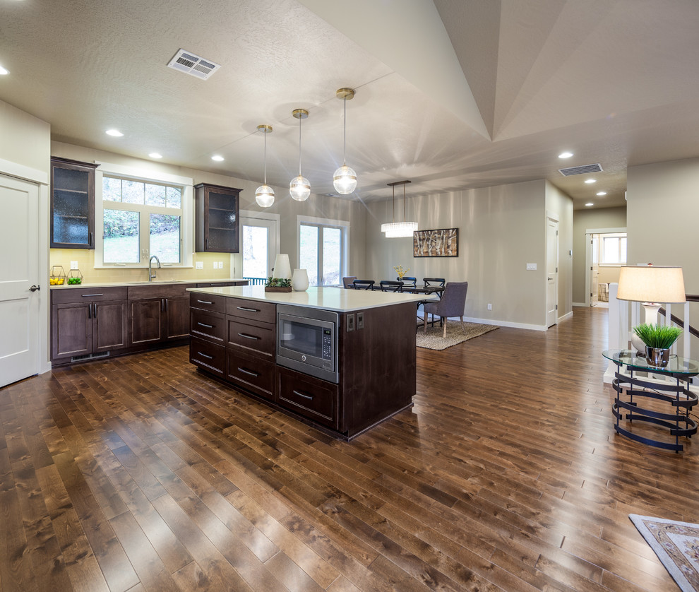 Inspiration for a mid-sized transitional l-shaped medium tone wood floor eat-in kitchen remodel with an undermount sink, recessed-panel cabinets, dark wood cabinets, solid surface countertops, beige backsplash, porcelain backsplash, paneled appliances and an island