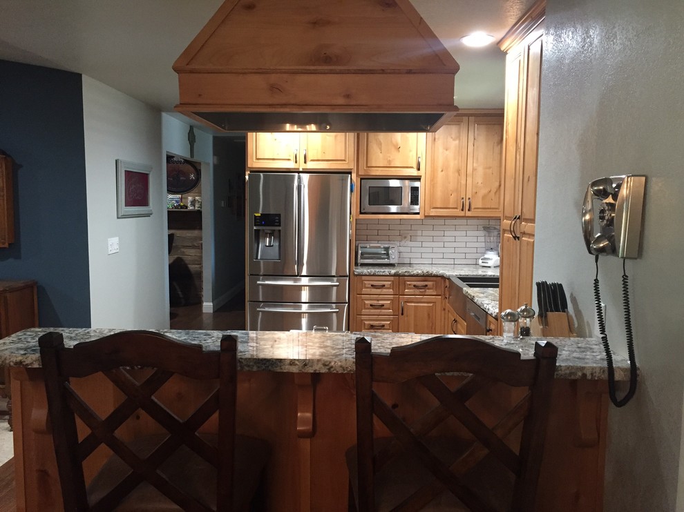 Mid-sized mountain style u-shaped medium tone wood floor kitchen photo with an undermount sink, raised-panel cabinets, light wood cabinets, granite countertops, white backsplash, ceramic backsplash and stainless steel appliances