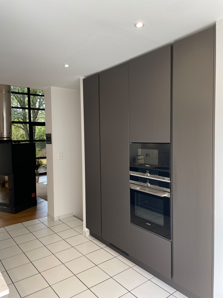 This is an example of a large modern single-wall open plan kitchen with an integrated sink, beaded inset cabinets, quartzite benchtops, white splashback, ceramic splashback, panelled appliances, ceramic floors, white floor, white benchtop and stainless steel cabinets.