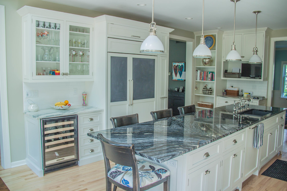 This is an example of a large transitional u-shaped eat-in kitchen in Milwaukee with white cabinets, marble benchtops, white splashback, stainless steel appliances, light hardwood floors, with island, an undermount sink, shaker cabinets, subway tile splashback, brown floor and black benchtop.