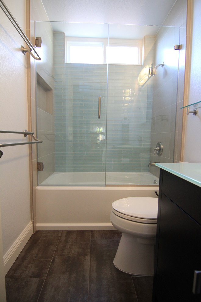 Photo of a small contemporary bathroom in Orange County with an integrated sink, flat-panel cabinets, dark wood cabinets, glass benchtops, an alcove tub, a shower/bathtub combo, a two-piece toilet, blue tile, glass tile, blue walls and porcelain floors.