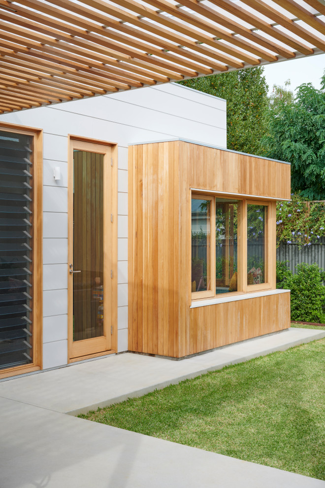 This is an example of a small contemporary one-storey grey house exterior in Adelaide with wood siding, a flat roof, a metal roof, a grey roof and board and batten siding.