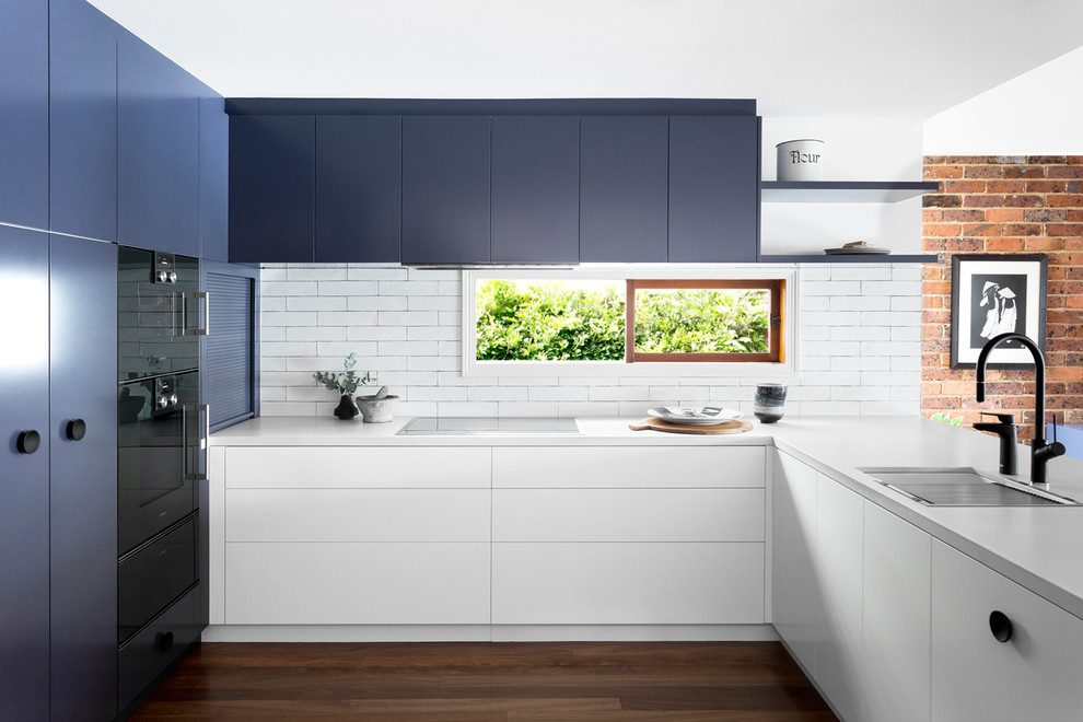 Mid-sized contemporary u-shaped eat-in kitchen in Melbourne with an undermount sink, flat-panel cabinets, blue cabinets, white splashback, black appliances, dark hardwood floors, quartz benchtops and window splashback.