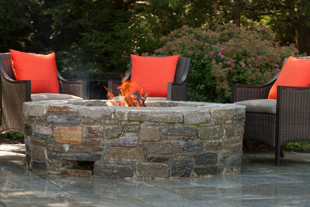 This is an example of a mid-sized country backyard patio in New York with a fire feature, natural stone pavers and no cover.