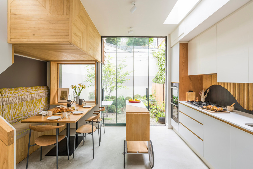 Photo of a mid-sized contemporary galley eat-in kitchen in London with a drop-in sink, flat-panel cabinets, white cabinets, solid surface benchtops, brown splashback, timber splashback, concrete floors, with island, white benchtop and white floor.