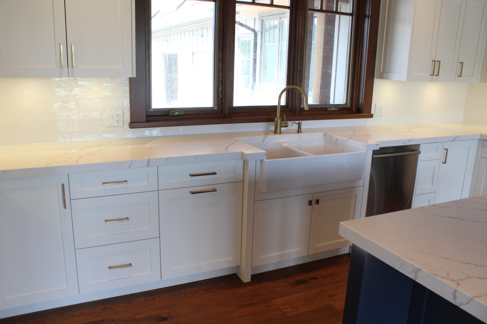 Example of a large mountain style u-shaped dark wood floor, brown floor and wood ceiling eat-in kitchen design in Toronto with a farmhouse sink, shaker cabinets, white cabinets, quartz countertops, white backsplash, subway tile backsplash, stainless steel appliances, an island and white countertops