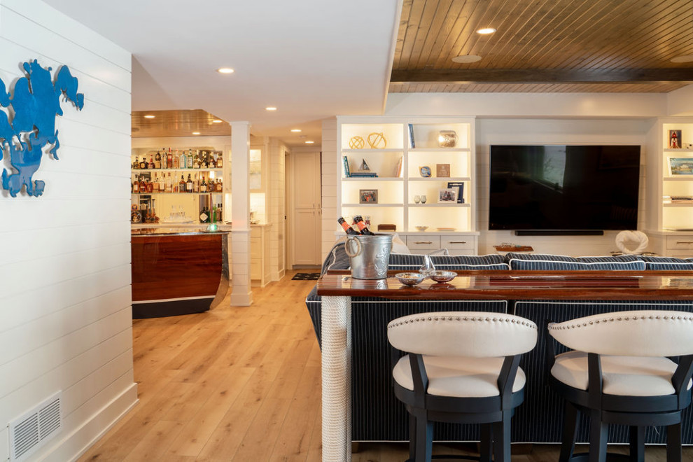Example of a mid-sized beach style walk-out light wood floor, brown floor, exposed beam and shiplap wall basement design in Minneapolis with a bar, white walls, a standard fireplace and a stone fireplace