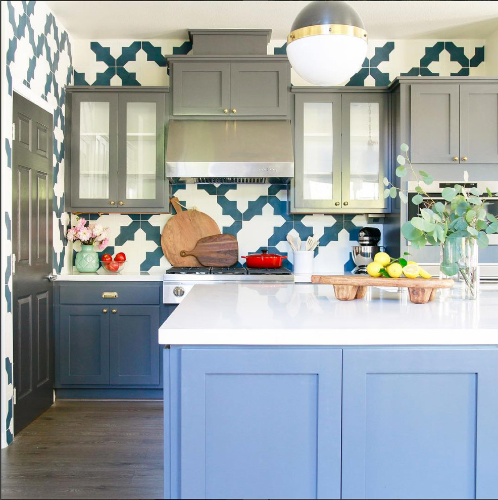 Photo of an eclectic u-shaped kitchen pantry in Los Angeles with with island, shaker cabinets, grey cabinets, solid surface benchtops, multi-coloured splashback, cement tile splashback, stainless steel appliances, laminate floors, grey floor and white benchtop.