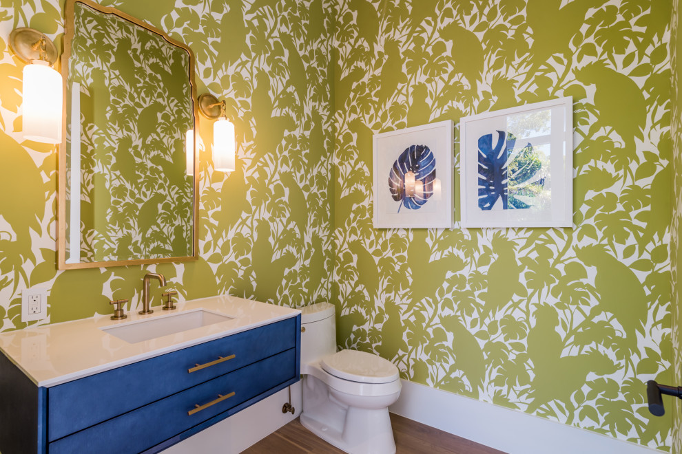 Photo of a mid-sized beach style bathroom in Miami with flat-panel cabinets, blue cabinets, a one-piece toilet, green walls, medium hardwood floors, an undermount sink, brown floor and white benchtops.