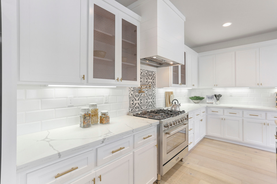 Photo of a large country l-shaped eat-in kitchen in Sacramento with a drop-in sink, shaker cabinets, white cabinets, quartz benchtops, white splashback, ceramic splashback, stainless steel appliances, light hardwood floors, with island, white floor and white benchtop.