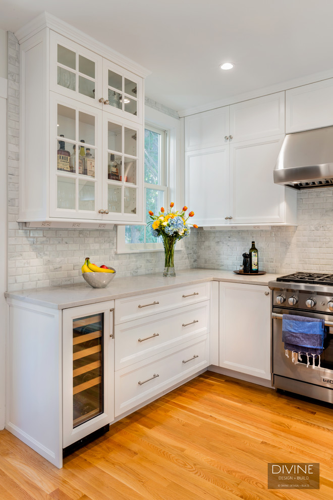 Eat-in kitchen - mid-sized transitional galley medium tone wood floor and brown floor eat-in kitchen idea in Boston with a farmhouse sink, shaker cabinets, white cabinets, marble countertops, multicolored backsplash, marble backsplash, stainless steel appliances and an island