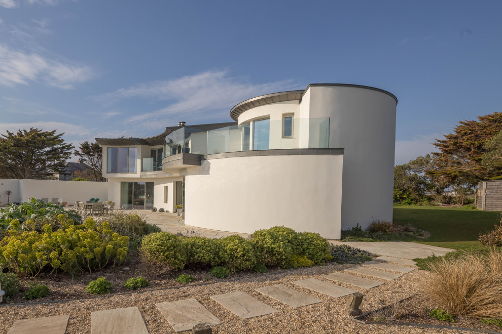 Photo of a large contemporary two-storey stucco white house exterior in Cornwall with a flat roof, a metal roof and a grey roof.