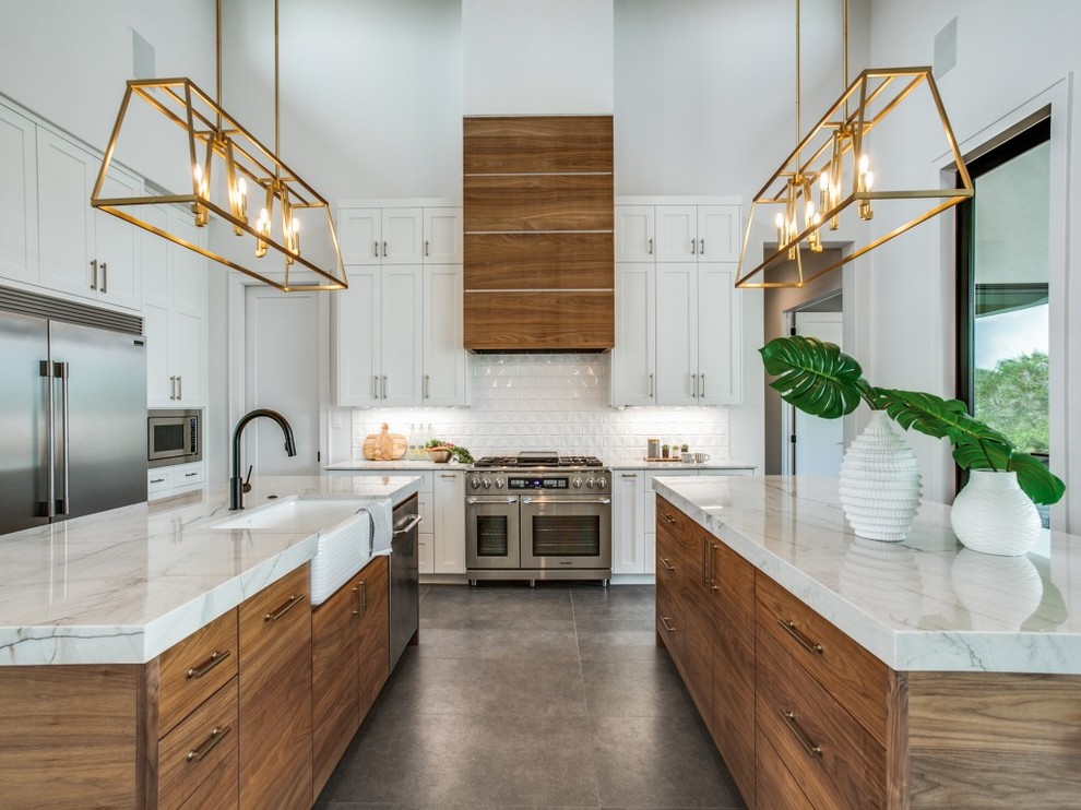 Large eclectic u-shaped open plan kitchen in Houston with a farmhouse sink, shaker cabinets, white cabinets, quartzite benchtops, white splashback, subway tile splashback, stainless steel appliances, porcelain floors, multiple islands, grey floor and white benchtop.
