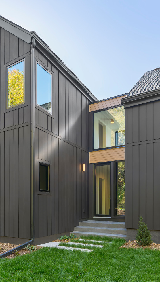 Large and black scandinavian two floor detached house in Minneapolis with wood cladding, a pitched roof, a shingle roof, a black roof and board and batten cladding.