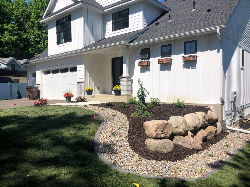 Large transitional front yard garden in Minneapolis with a retaining wall and river rock.