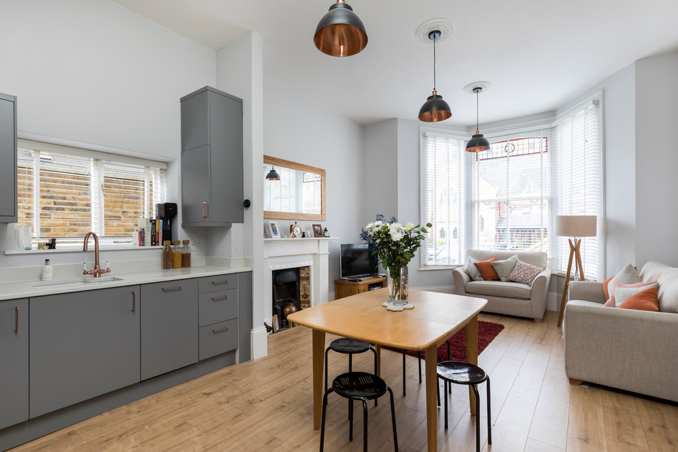 Small arts and crafts l-shaped open plan kitchen in London with an integrated sink, flat-panel cabinets, grey cabinets, solid surface benchtops, white splashback, limestone splashback, stainless steel appliances, laminate floors and no island.