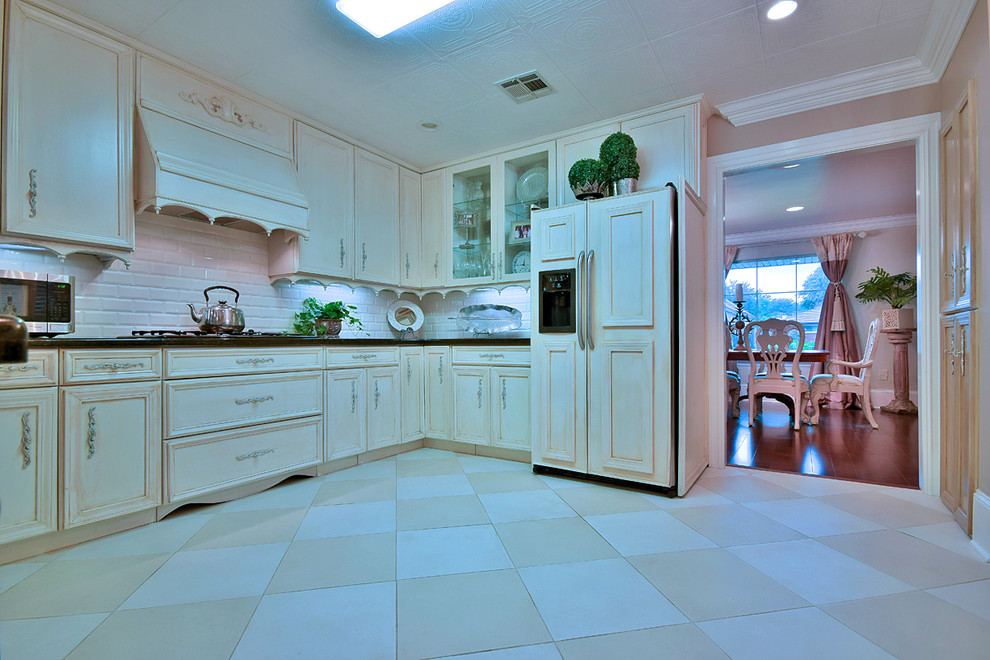 Large u-shaped eat-in kitchen in New Orleans with white cabinets, granite benchtops, white splashback, porcelain floors, a drop-in sink, recessed-panel cabinets, subway tile splashback, panelled appliances, a peninsula and black floor.