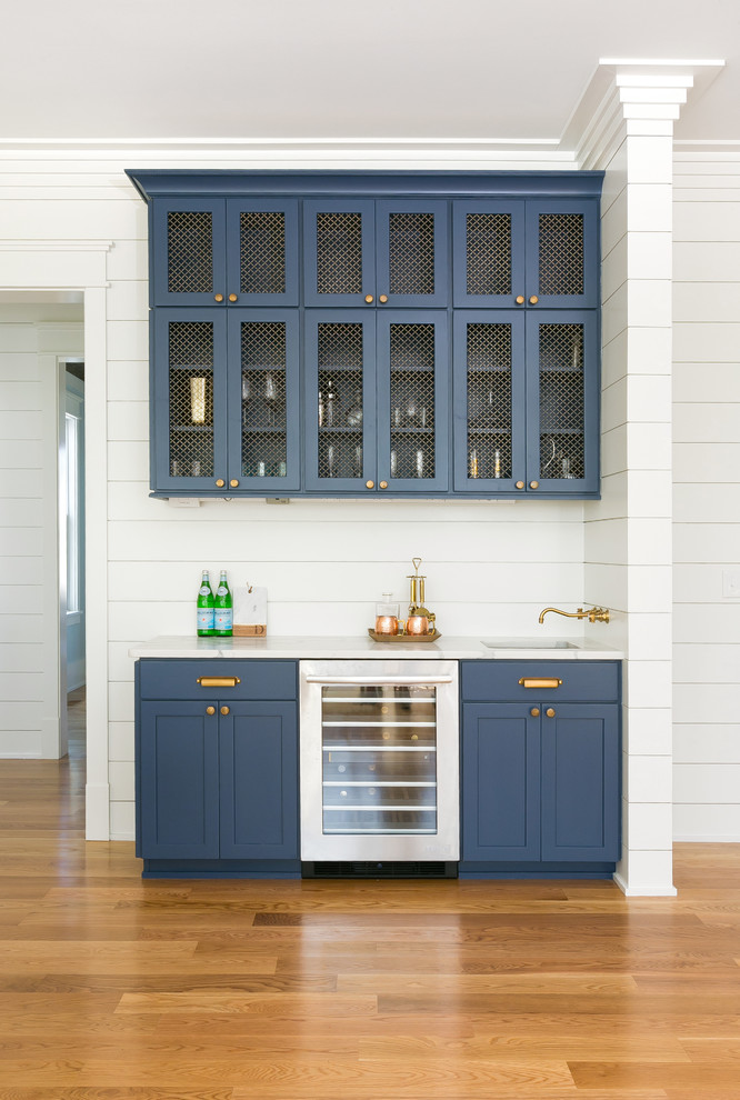 This is an example of a mid-sized country single-wall wet bar in Charleston with blue cabinets, white benchtop, an undermount sink, recessed-panel cabinets, marble benchtops, white splashback, timber splashback, medium hardwood floors and brown floor.